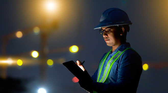 Ingénieur de construction utilisant sa tablette industrielle sur un chantier, de nuit