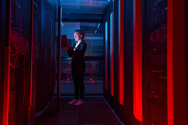 Technicienne d’une société prestataire de service informatique, vêtue de noir, debout dans un data center avec un ordinateur